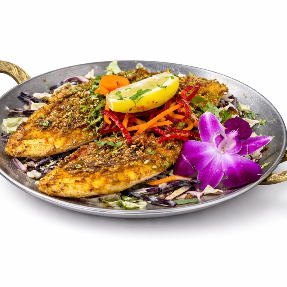 Two seasoned grilled fish fillets served over shredded salad with colorful vegetables, lemon, herbs, and a purple orchid garnish.