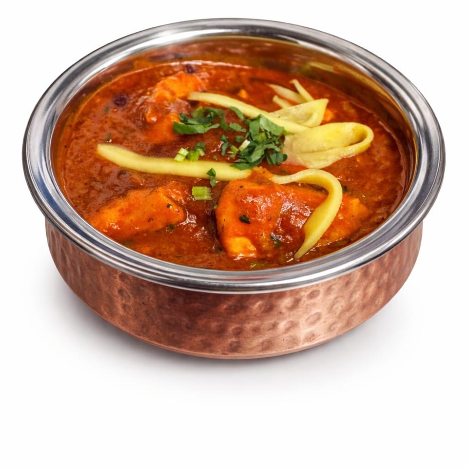 Copper bowl of creamy red curry with paneer pieces, ginger strips, and cilantro garnish.