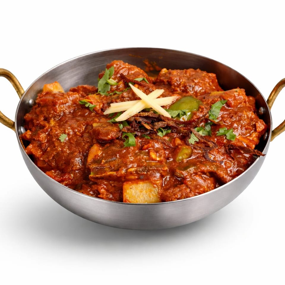 Rich red Indian curry garnished with cilantro, ginger strips, chilies, and fried onions in a handled metal serving pan.
