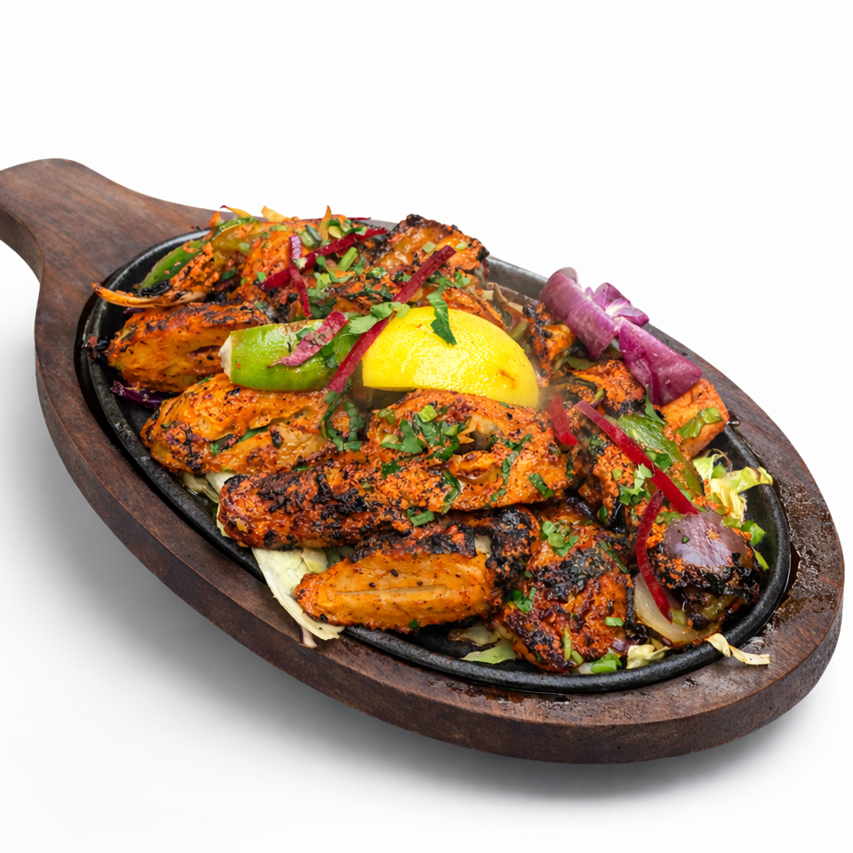 Grilled orange-marinated chicken pieces topped with herbs, pickled onions, lime, and lemon on a sizzling wooden platter.